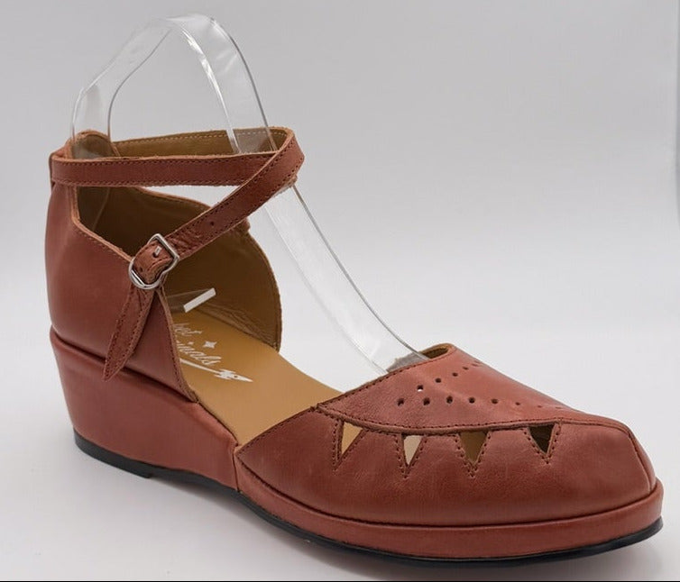 A single women's wedge sandal in a warm rust-brown colour.  The sandal features a cutout toe, a criss cross with a buckle, and a low wedge heel.
