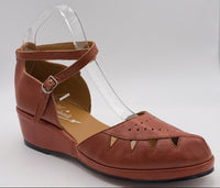 A single women's wedge sandal in a warm rust-brown colour.  The sandal features a cutout toe, a criss cross with a buckle, and a low wedge heel.