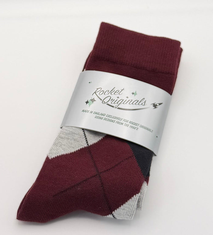 A folded pair of burgundy argyle socks with a silver paper band label.