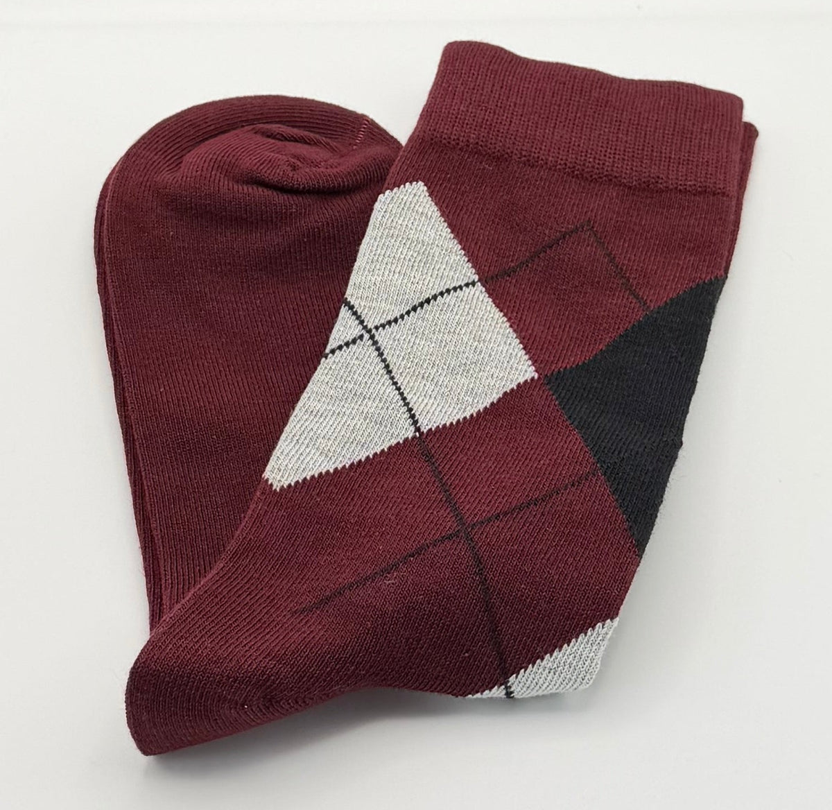 A folded pair of burgundy argyle socks with white and black details.